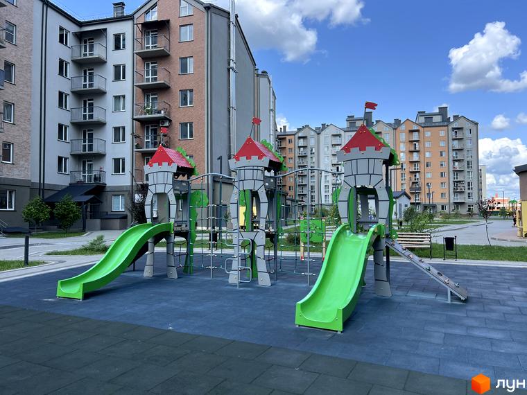 Житловий комплекс Scandia. Сучасний дитячий майданчик з гірками та елементами замку на тлі багатоповерхових будинків.