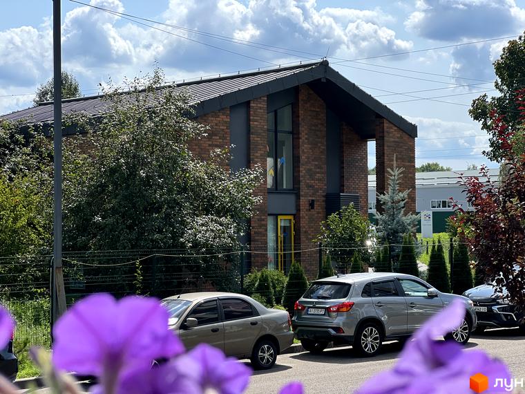 Будинок ЖК Scandia з цегляним фасадом та великими вікнами, поруч зелені насадження та припарковані автомобілі.