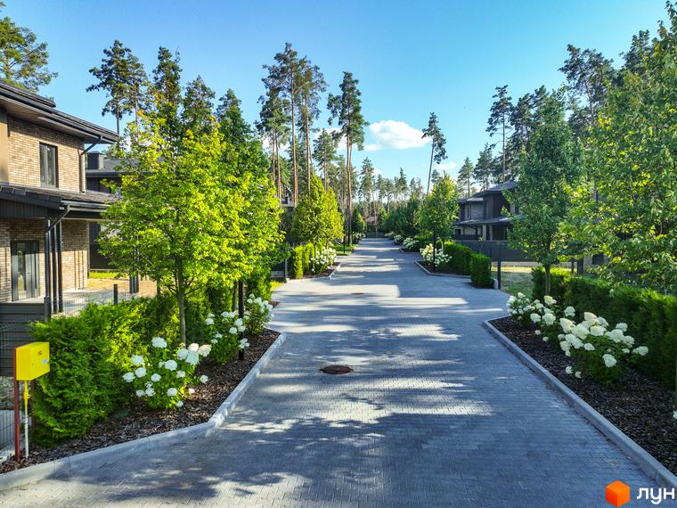 Котеджне містечко ZAHRAVA village 2. Асфальтована дорога з бруківкою, огороджена парканом, з зеленими деревами та кущами.