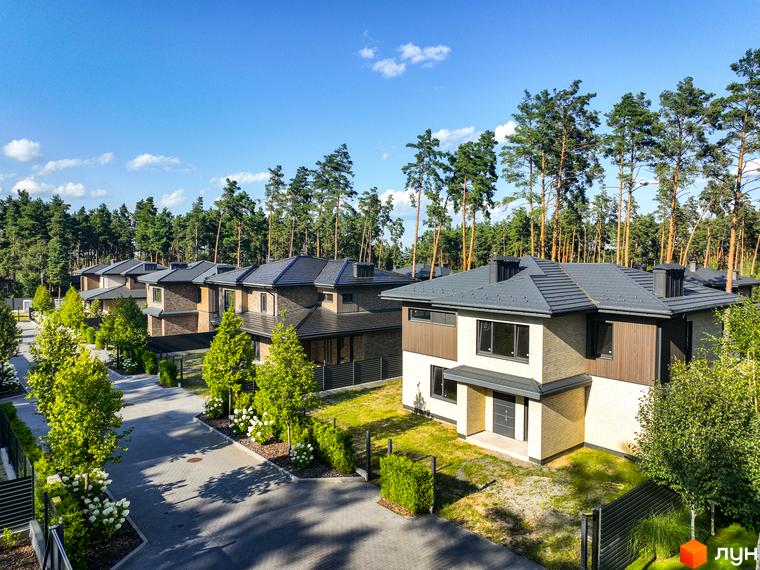 Котеджне містечко ZAHRAVA village 2. Зовнішній вигляд двоповерхових будинків з цегляним та дерев'яним оздобленням, сірими дахами та великими вікнами, розташованих на фоні соснового лісу.