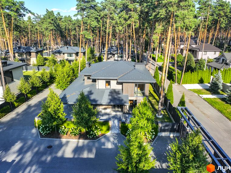 Котеджне містечко ZAHRAVA village 2. Зовнішній вигляд двоповерхового будинку з сірим дахом та цегляними стінами, прибудинкова територія з зеленими деревами та бруківкою.