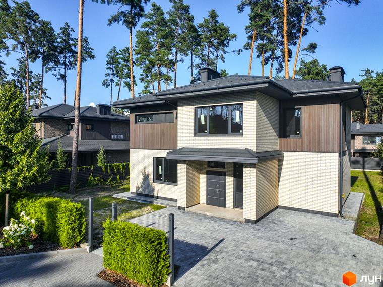 Котеджне містечко ZAHRAVA village 2. Зовнішній вигляд двоповерхового будинку з цегляним фасадом та дерев'яними елементами, прибудинкова територія з доглянутими кущами та бруківкою.