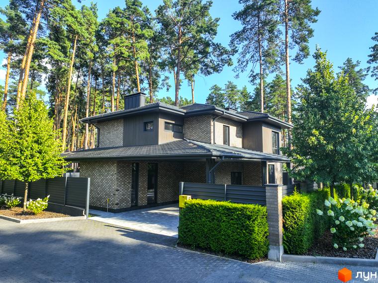 Котеджне містечко ZAHRAVA village 2 – двоповерховий будинок з цегляним фасадом та навісом для авто, оточений зеленню та хвойними деревами.