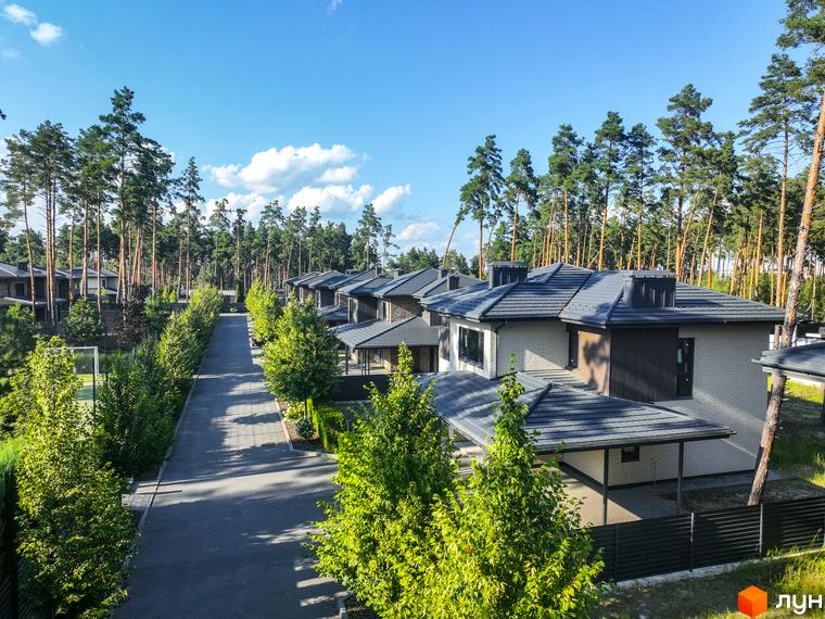 Котеджне містечко ZAHRAVA village 2 з сірими дахами та цегляними фасадами, розташоване серед високих сосен. На території комплексу асфальтована дорога та зелені насадження.