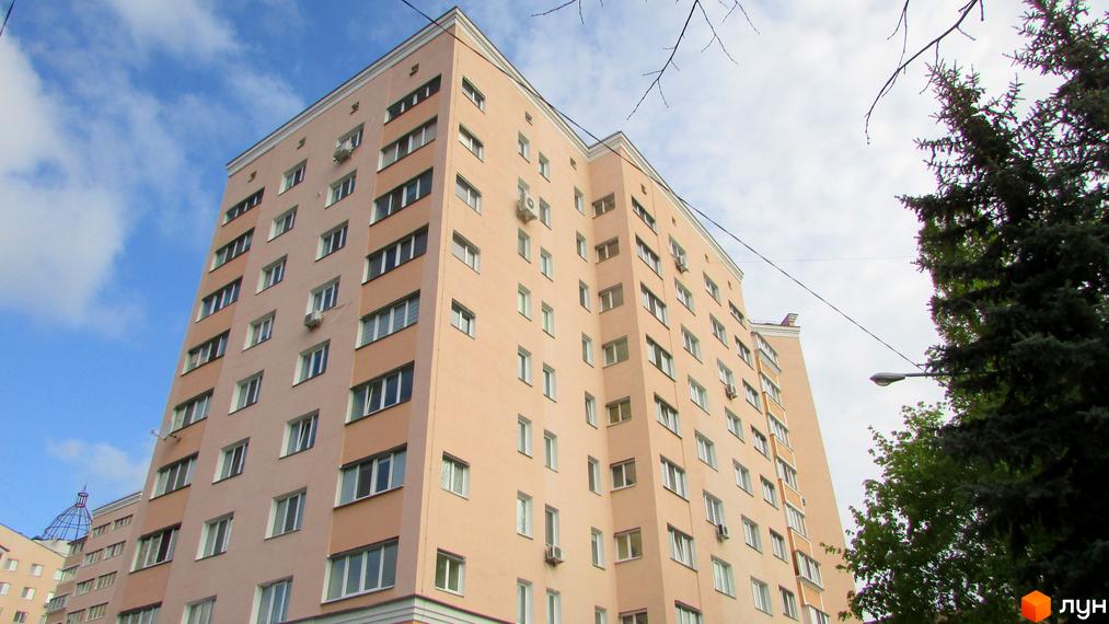 Фасад будинку на просп. Шевченка, 6а, у Львові. Багатоповерхівка з світло-персиковими стінами та численними вікнами. Навколо будинку зелені дерева та блакитне небо з хмарами.