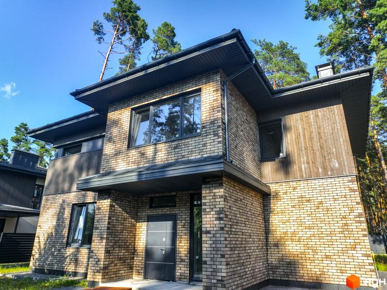 Котеджне містечко ZAHRAVA village 2: двоповерховий будинок з цегляним фасадом та дерев'яними елементами, вікна, двері, дах, дерева на фоні блакитного неба.