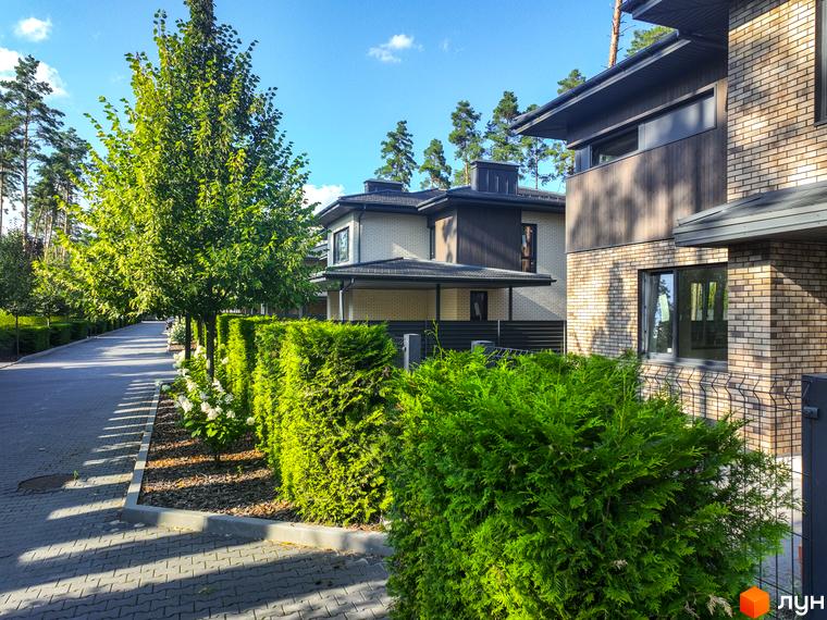 Котеджне містечко ZAHRAVA village 2: фасади будинків з цегли та дерева, доглянута прибудинкова територія з акуратними кущами та деревами.