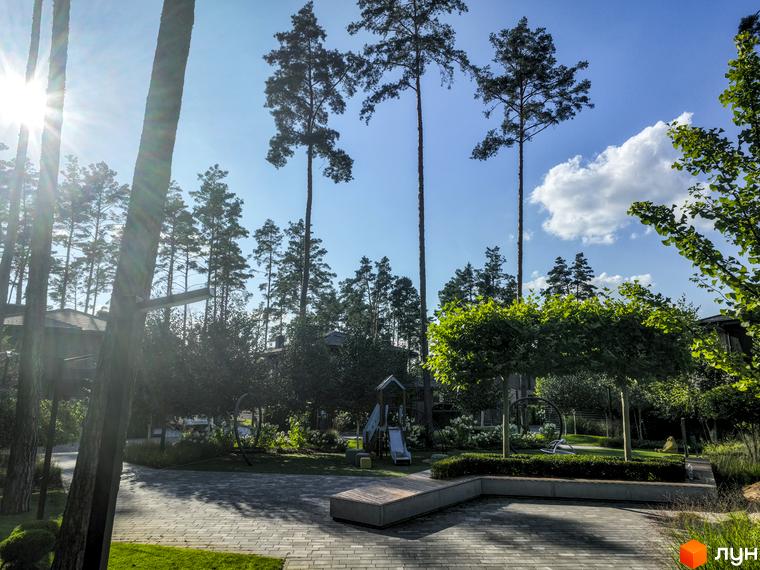Котеджне містечко КМ ZAHRAVA village 2 з високими соснами та дитячим майданчиком. Зелена прибудинкова територія з доріжками та лавками.