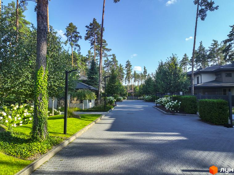 Котеджне містечко ZAHRAVA village 2. Асфальтована дорога з бруківкою веде до будинків, оточених зеленню та квітами.