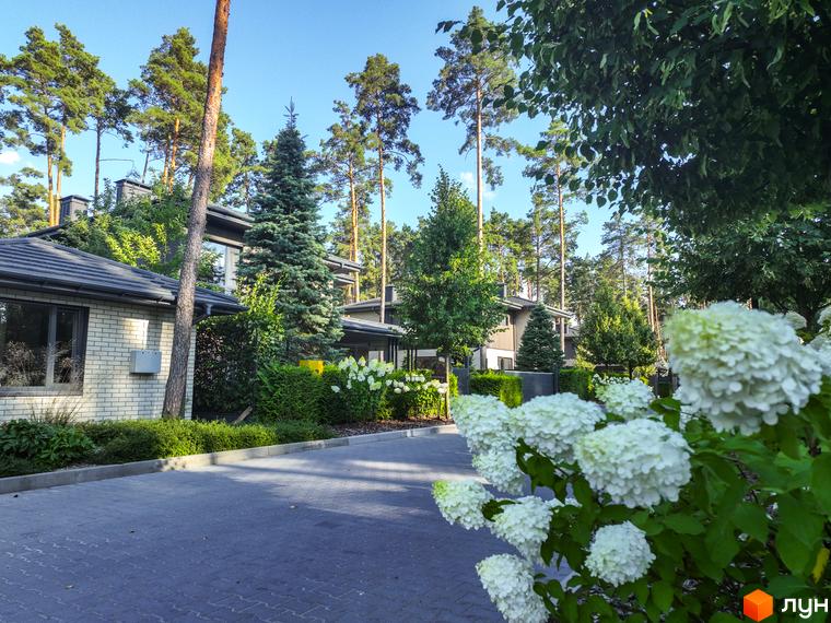 Котеджне містечко ZAHRAVA village 2 з цегляними фасадами та доглянутою зеленою територією. На передньому плані білі квіти та бруківка.
