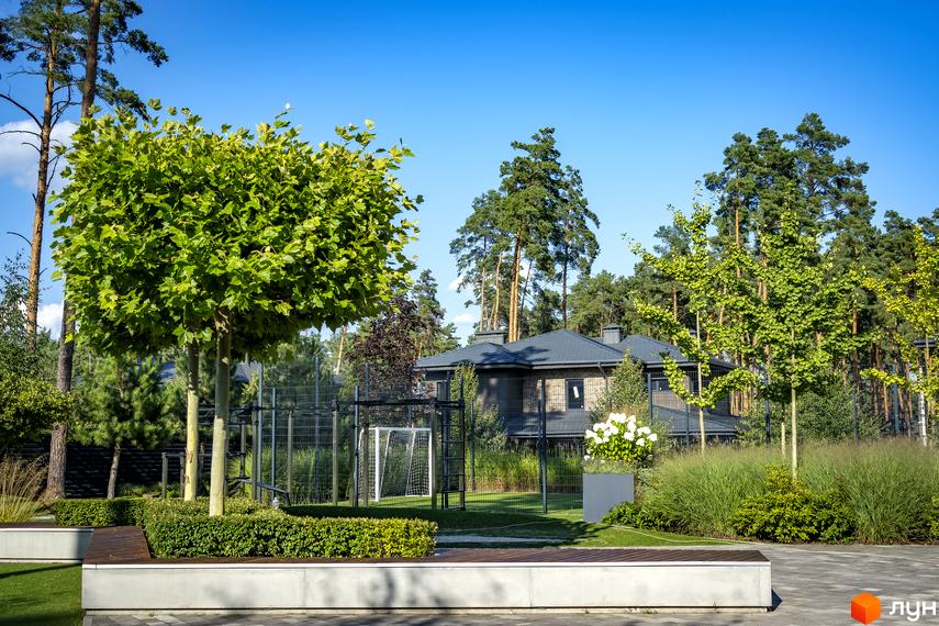 Котеджне містечко КМ ZAHRAVA village 2: двоповерховий будинок з сірим дахом та цегляним фасадом, оточений зеленню та спортивним майданчиком.