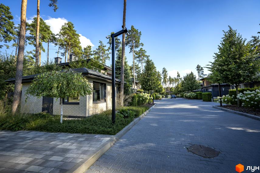 Котеджне містечко ZAHRAVA village 2. Затишна вулиця з бруківкою та будинками, оточена деревами та зеленню.