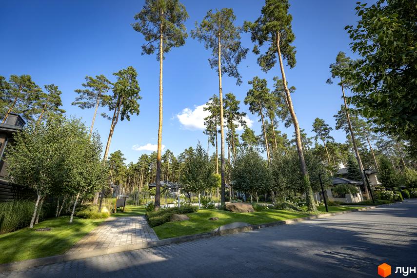 Котеджне містечко ZAHRAVA village 2. Будинки з темними фасадами та сірими дахами розташовані серед високих сосен, з доглянутими газонами та брукованими доріжками.