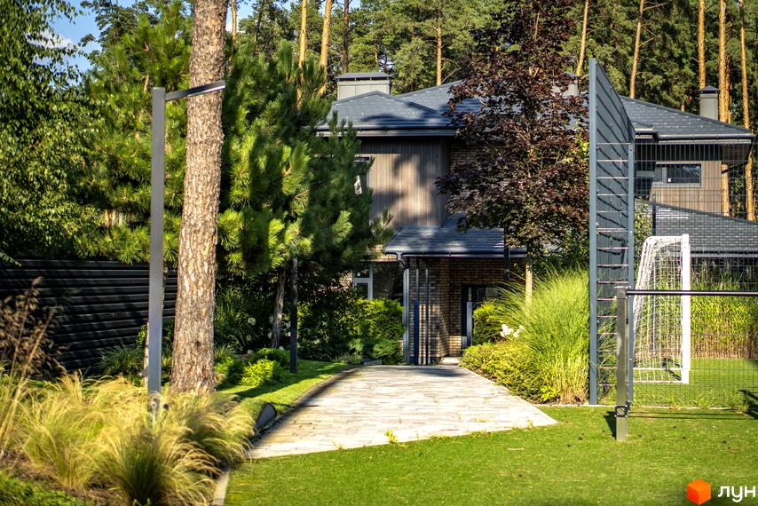 Котеджне містечко ZAHRAVA village 2. Зовнішній вигляд будинку з цегляним фасадом та сірим дахом, прибудинкова територія з доріжкою та зеленню.