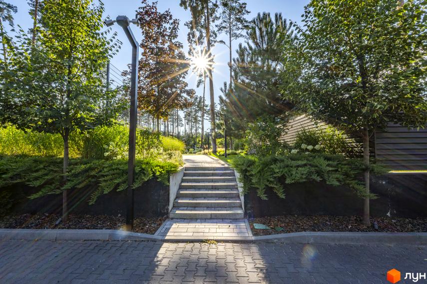 Котеджне містечко ZAHRAVA village 2. Сходи, що ведуть до будинку, оточені зеленню та деревами під яскравим сонцем.