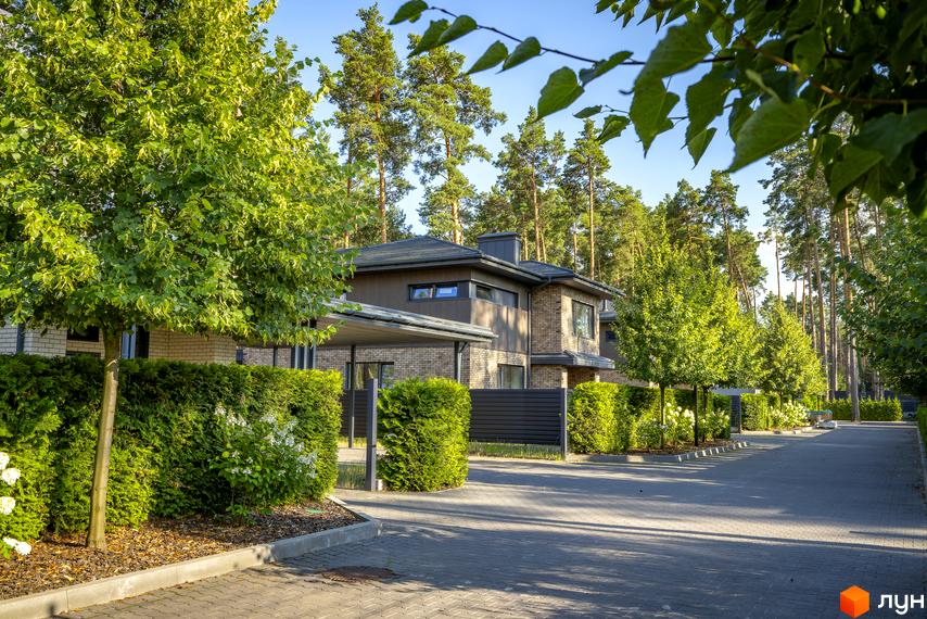 Котеджне містечко ZAHRAVA village 2. Фасад будинку з цегли та дерева, навіс для авто, зелені насадження та бруківка.