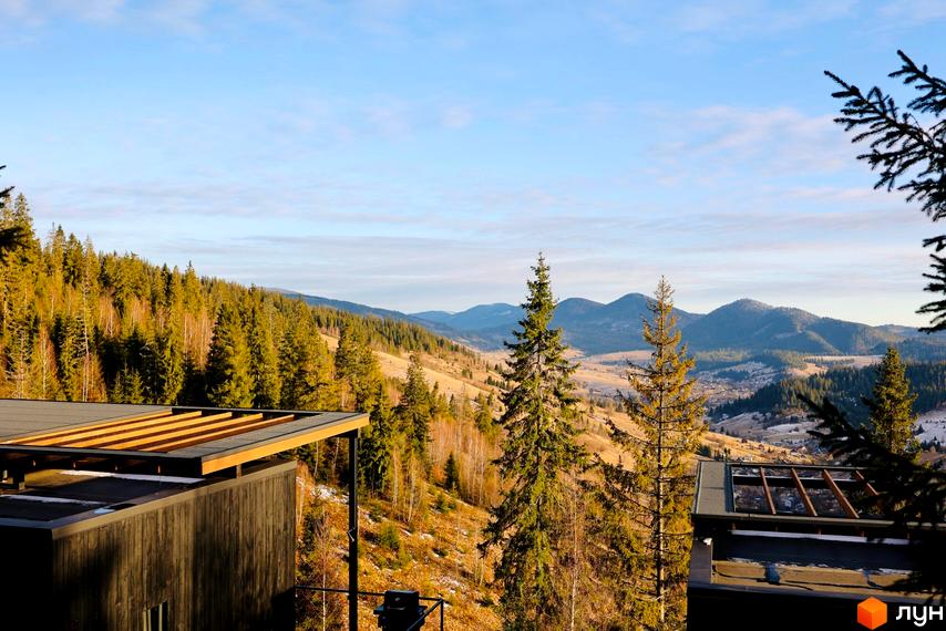 Котеджне містечко КМ Висота 890 з дерев'яними елементами на даху та темними фасадами, оточене гірським лісом та долиною.