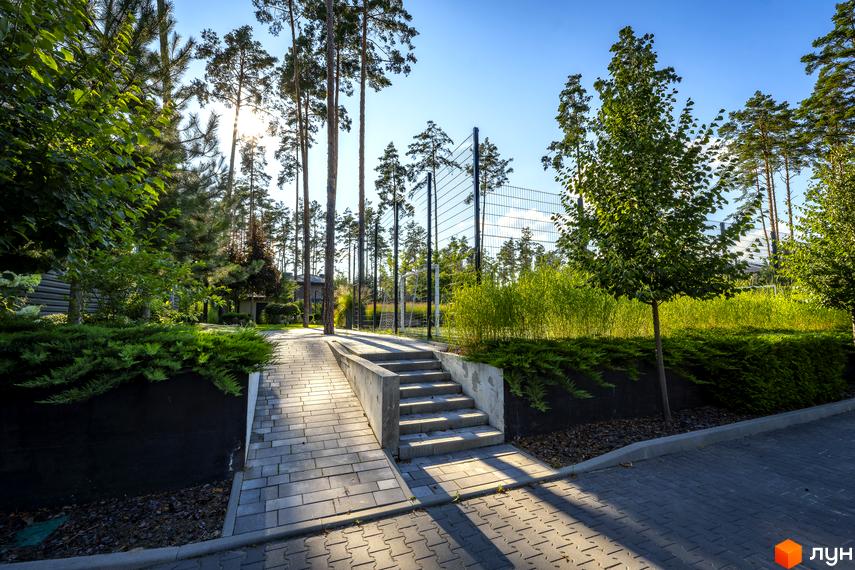 КМ ZAHRAVA village 2: доглянута прибудинкова територія з бруківкою, сходами та зеленню біля паркану.