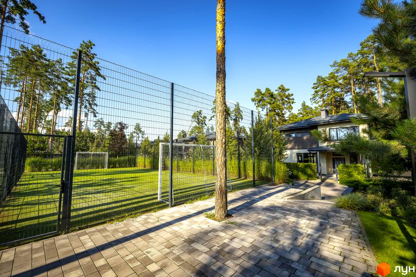 Котеджне містечко ZAHRAVA village 2. Зовнішній вигляд будинку з цегли та дерева, прибудинкова територія з футбольним полем та зеленими насадженнями.