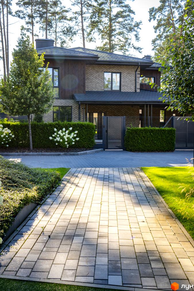 Котеджне містечко КМ ZAHRAVA village 2. Фасад будинку з цегли та дерева, доглянута прибудинкова територія з акуратними кущами та бруківкою.