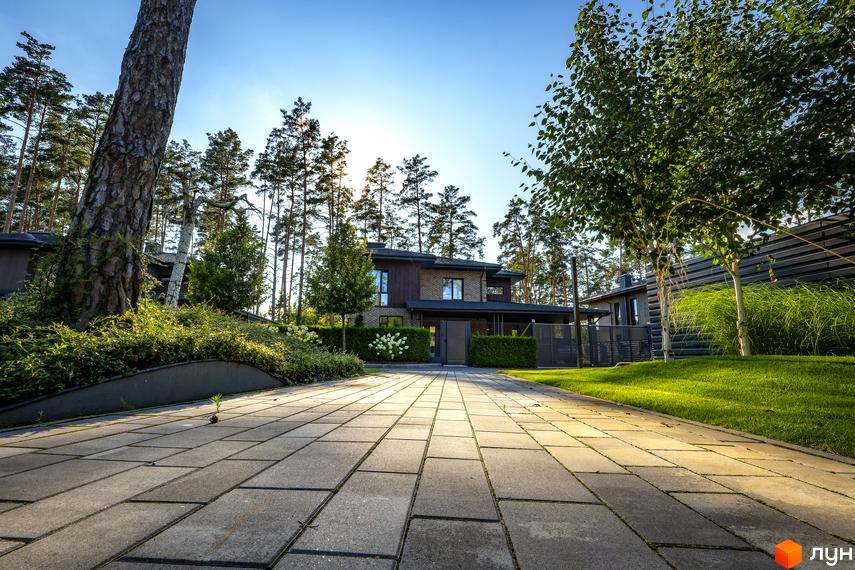 Котеджне містечко ZAHRAVA village 2. Зовнішній вигляд двоповерхового будинку з цегли та дерева, вхідна група з навісом, доглянута прибудинкова територія з газоном та деревами.