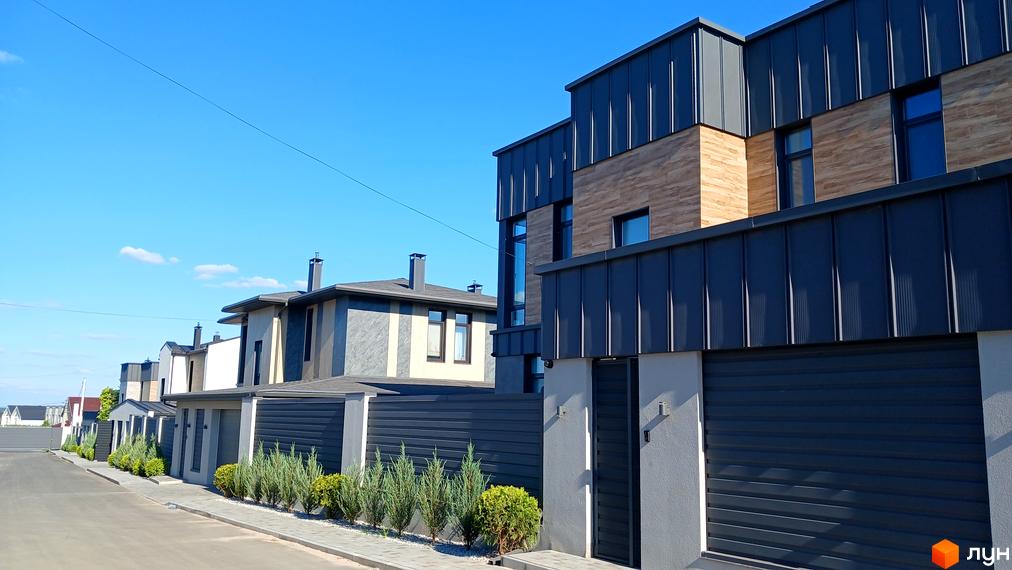 Новобудова на вул. Зелений Гай з сірим фасадом та темними вікнами, огороджена парканом, з акуратними зеленими насадженнями вздовж тротуару.