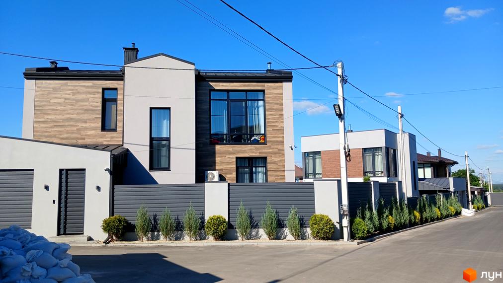 Фасад будинку з дерев'яними та сірими елементами на вулиці Зелений Гай. Озеленена прибудинкова територія з туями та кущами.