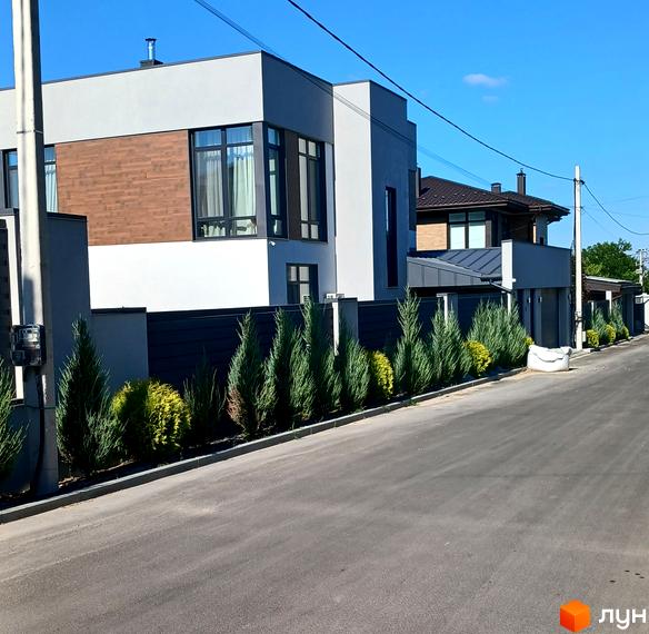 Зовнішній вигляд двоповерхового будинку з дерев'яними вставками та великими вікнами на вулиці Зелений Гай. Прибудинкова територія огороджена парканом та засаджена туями.