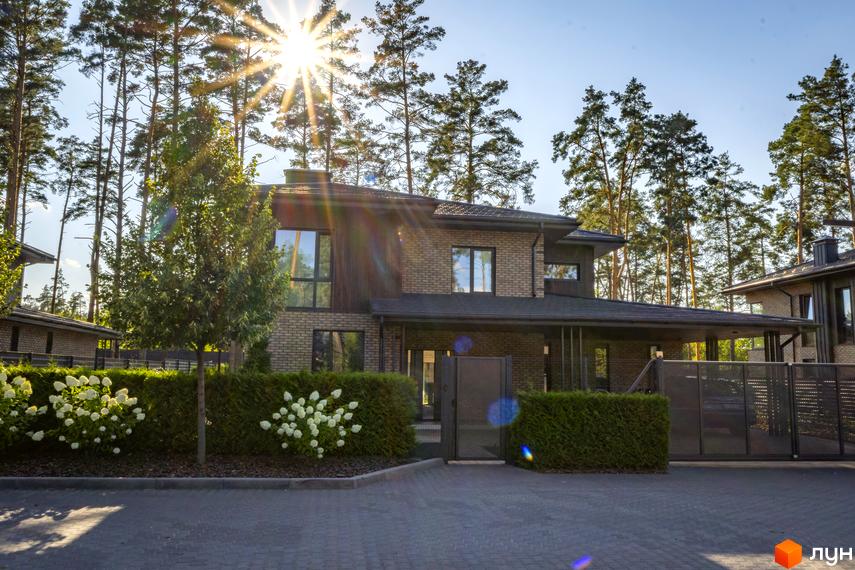 Котеджне містечко ZAHRAVA village 2. Фасад будинку з цегли та дерева, великі вікна, доглянута прибудинкова територія з кущами та деревами.