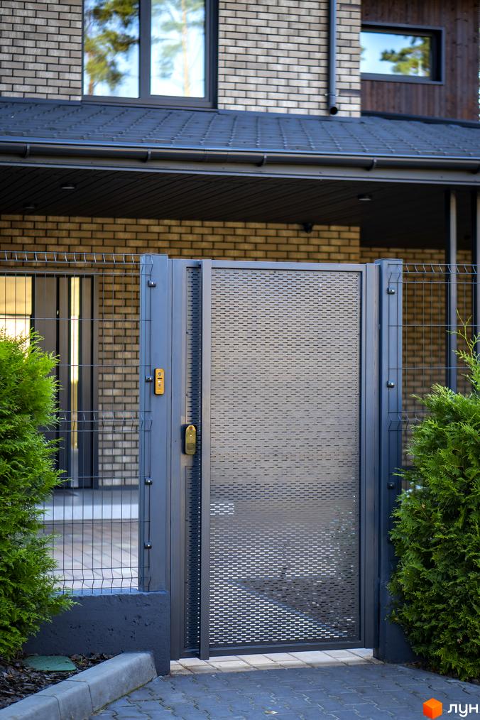 Котеджне містечко ZAHRAVA village 2: сіра металева брама з перфорацією та паркан з металевої сітки на фоні цегляного будинку.