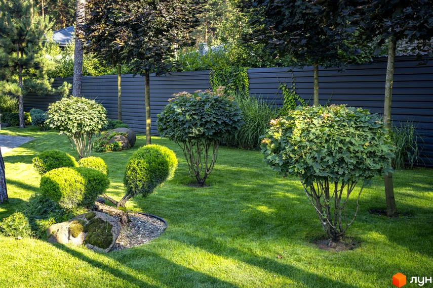 КМ ZAHRAVA village 2: доглянутий сад з акуратно підстриженими кущами та деревами, що оточують будинок. Зелений газон та кам'яні елементи ландшафтного дизайну.