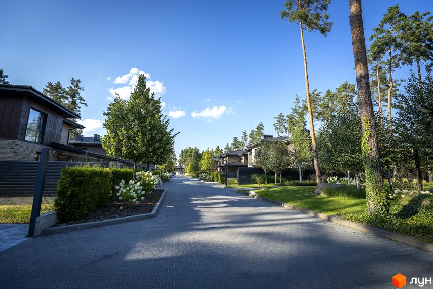 Котеджне містечко ZAHRAVA village 2: сучасні будинки з дерев'яним фасадом та цегляними елементами, розташовані вздовж доглянутої вулиці з газонами та деревами.