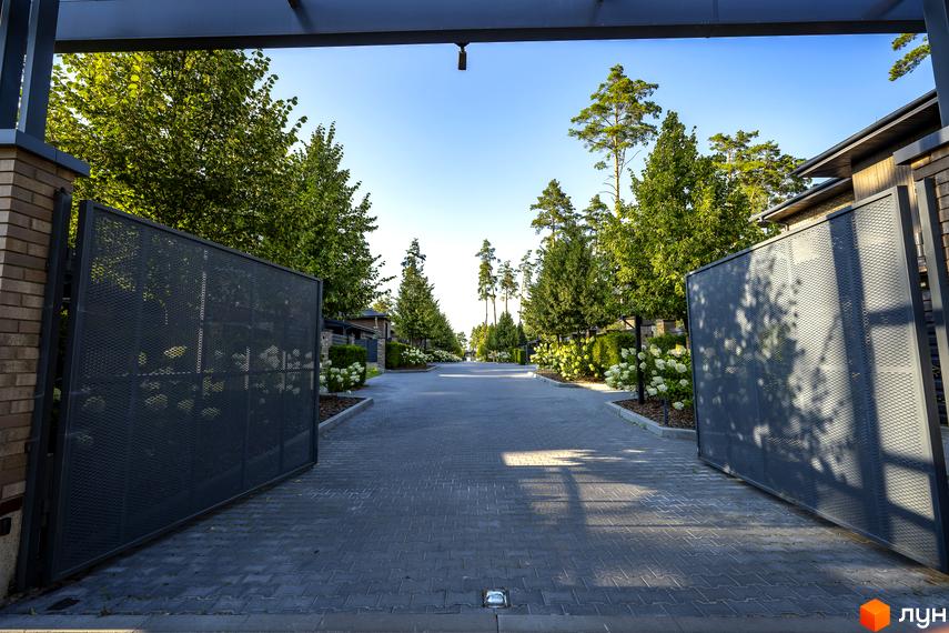 Котеджне містечко ZAHRAVA village 2: в'їзд на територію через відкриті ворота, асфальтована дорога, зелені насадження та квіти.