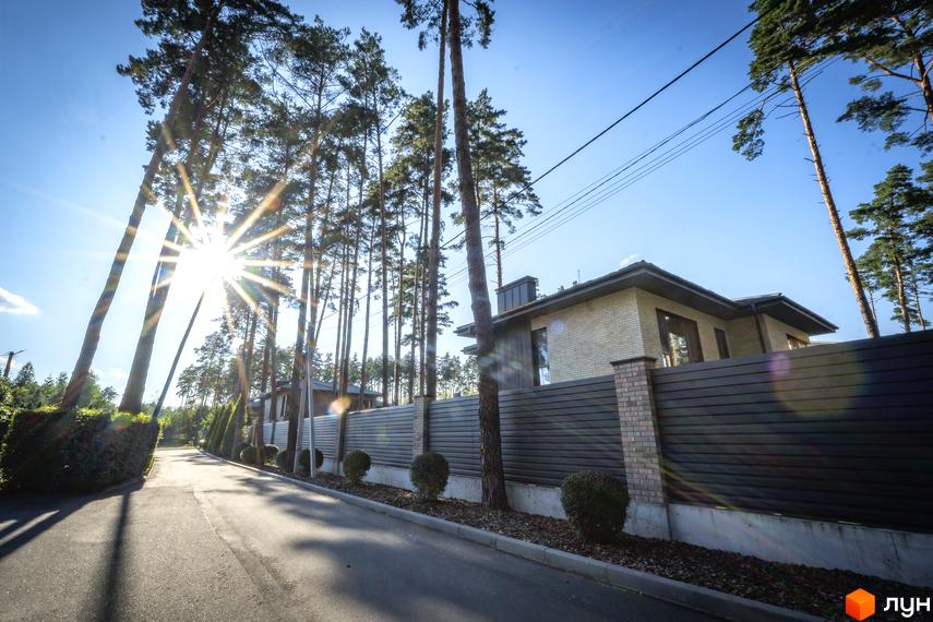 Котеджне містечко ZAHRAVA village 2. Зовнішній вигляд будинку з цегляним фасадом та темним парканом. Прибудинкова територія з доглянутими деревами та кущами.