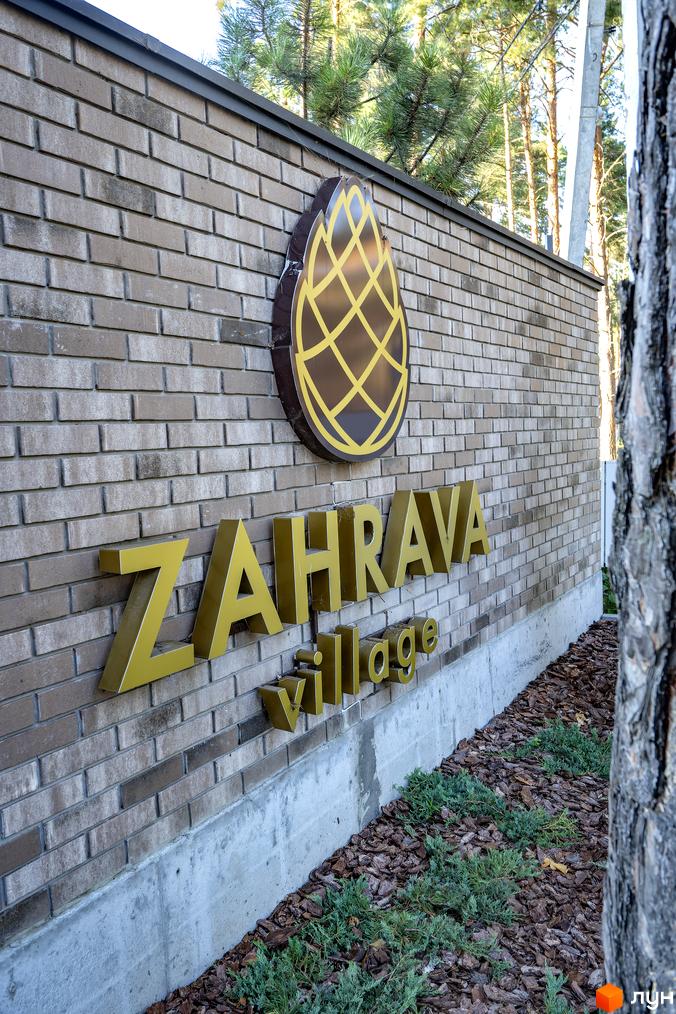 Котеджне містечко ZAHRAVA village з золотими об'ємними літерами на цегляній стіні. Навколо зелені насадження та кора дерева.