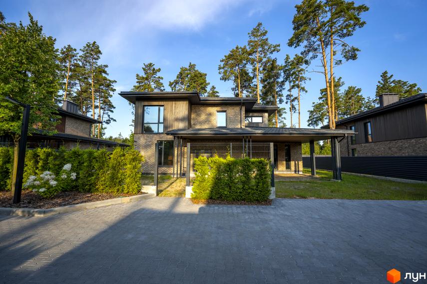 Котеджне містечко ZAHRAVA village 2. Фасад будинку з цегли та дерева, навіс для автомобілів, зелені насадження та вимощена сіра доріжка.