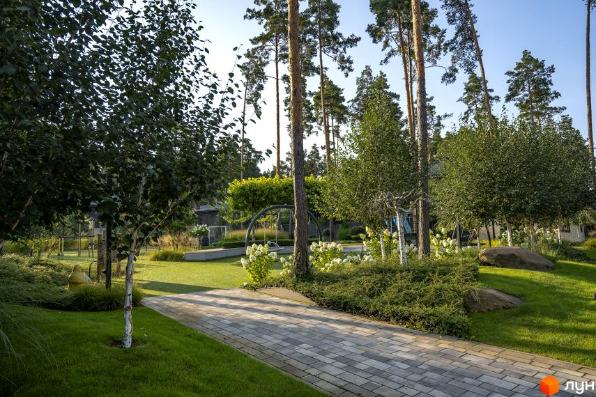 Котеджне містечко ZAHRAVA village 2: зелений ландшафт з доріжкою з плитки, деревами та кущами. Прибудинкова територія з газоном та елементами ландшафтного дизайну.