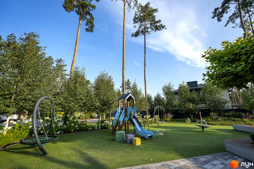Котеджне містечко ZAHRAVA village 2: дитячий майданчик з гіркою та гойдалками на зеленій галявині біля будинків.
