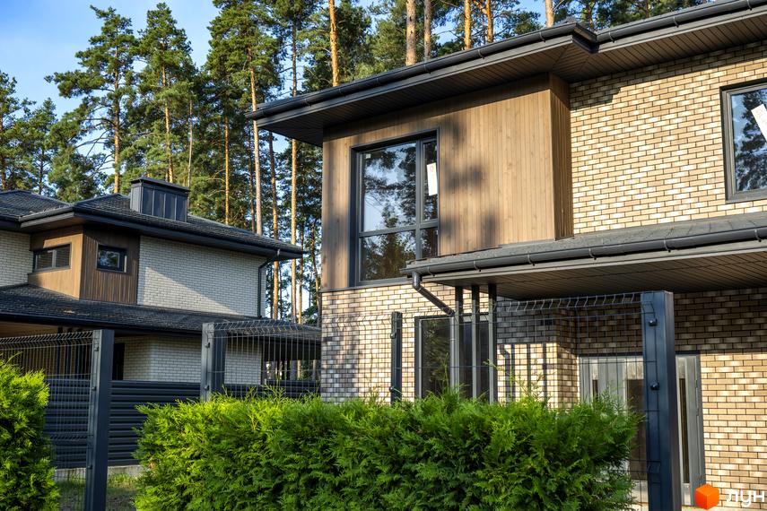 Котеджне містечко KМ ZAHRAVA village 2: двоповерхові будинки з цегляним фасадом та дерев'яними елементами, огороджена територія з кущами.