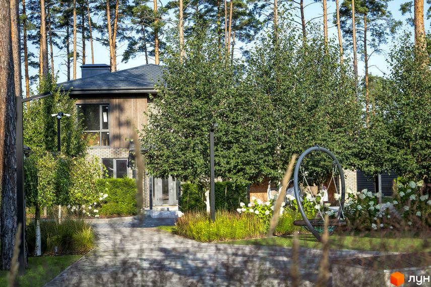 Котеджне містечко ZAHRAVA village 2: двоповерховий будинок з дерев'яним фасадом, цегляною кладкою та великими вікнами. На прибудинковій території - зелені насадження, доріжка та гойдалка.