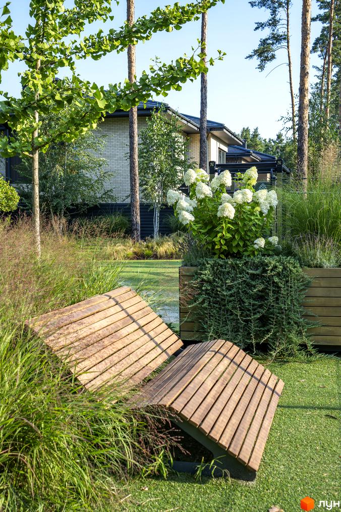 Котеджне містечко КМ ZAHRAVA village 2. Зелена прибудинкова територія з дерев'яними лавами та квітучими рослинами.