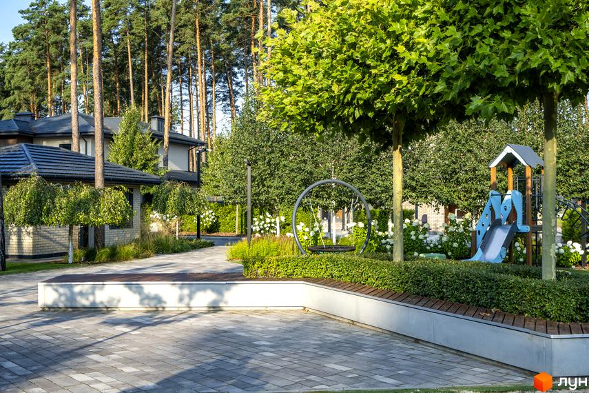Котеджне містечко ZAHRAVA village 2: сучасний дитячий майданчик з гіркою та гойдалкою на фоні будинків та зелених дерев.