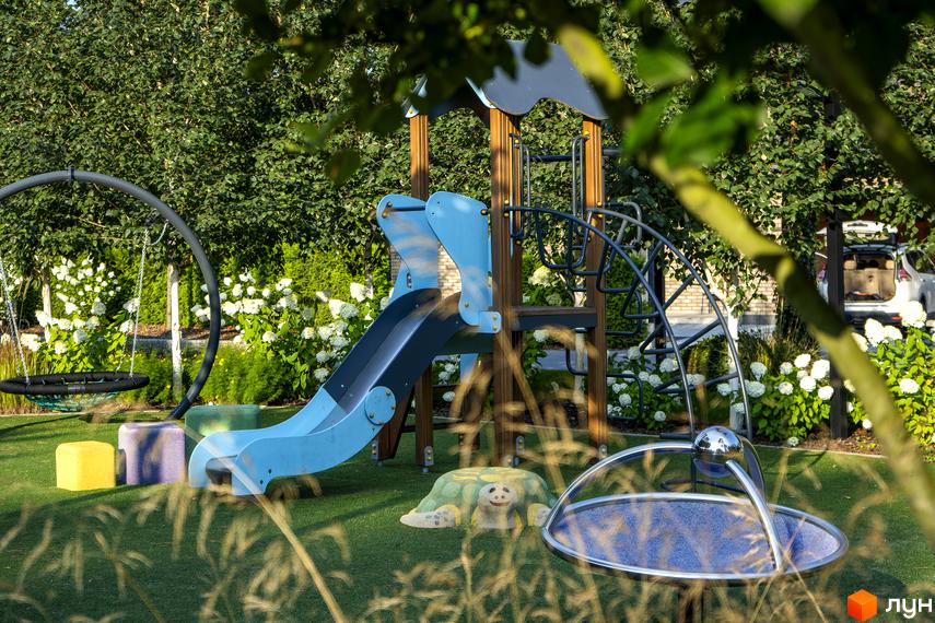 Дитячий майданчик з гіркою, гойдалкою та пісочницею на території житлового комплексу КМ ZAHRAVA village 2. Зелена зона з квітами та деревами.