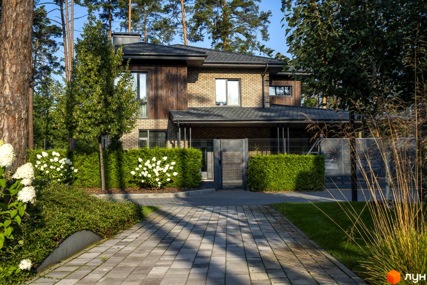 Котеджне містечко КМ ZAHRAVA village 2. Цегляний будинок з дерев'яними елементами та доглянутою прибудинковою територією з акуратними кущами та бруківкою.