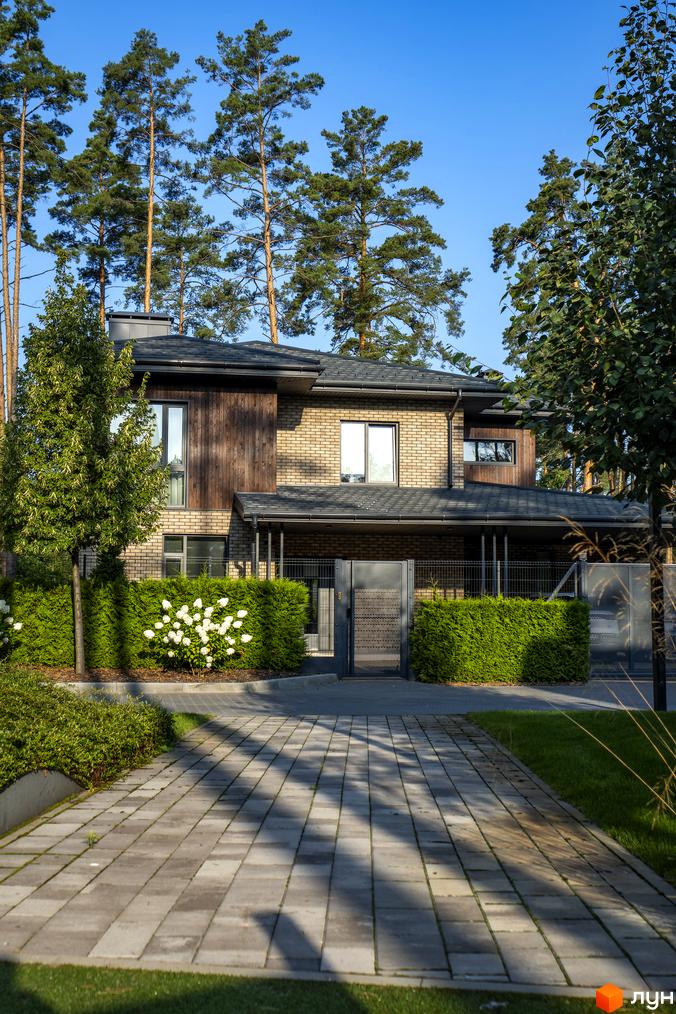 Котеджне містечко ZAHRAVA village 2: двоповерховий будинок з цегляним фасадом та дерев'яними елементами, зелений газон та вимощена доріжка перед будинком.