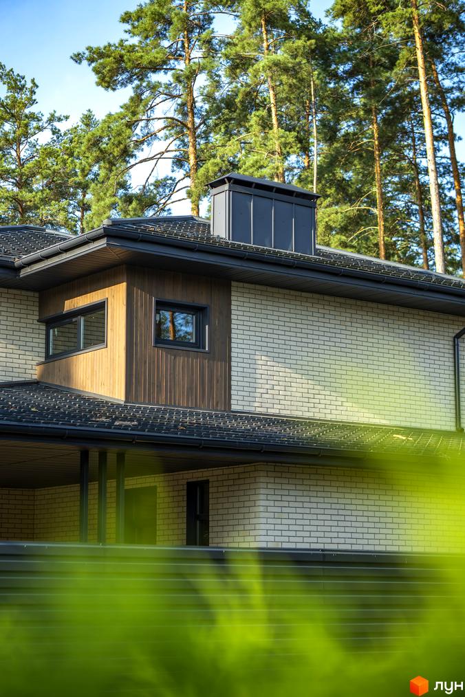 Котеджне містечко ZAHRAVA village 2: двоповерховий будинок з цегляним фасадом, дерев'яними елементами та темним дахом на тлі соснового лісу.