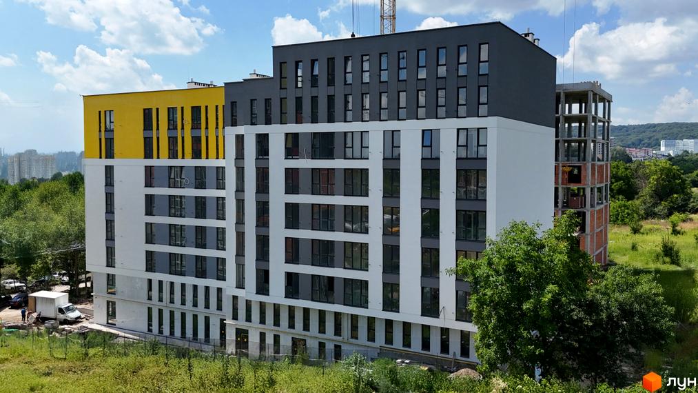 Зовнішній вигляд новобудови ЖК Весняний з жовтими та сірими фасадами, вікнами та прибудинковою територією.