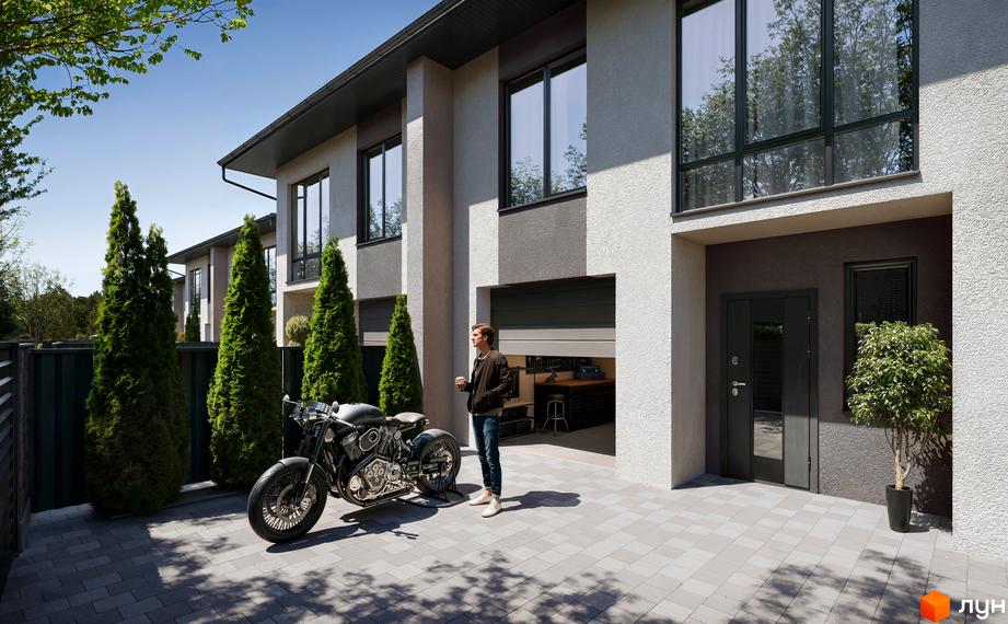 Котеджне містечко КМ WEST TOWN XIV. Зовнішній вигляд будинку з гаражем, мотоциклом та чоловіком біля нього.