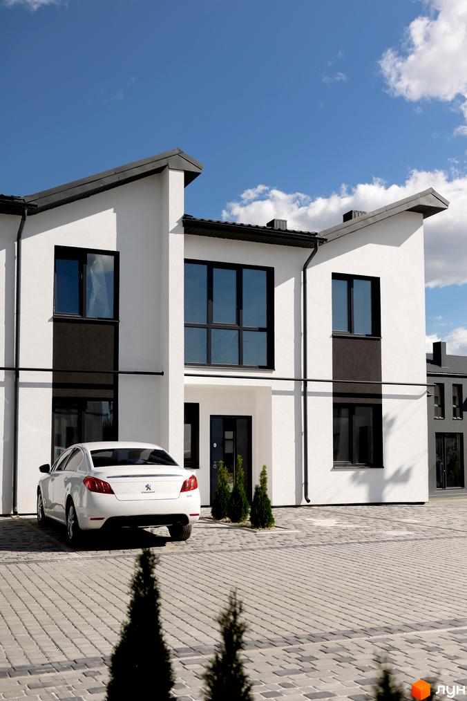 Котеджне містечко КМ WEST TOWN XIV. Білий будинок з чорними вікнами та дахом, прибудинкова територія з бруківкою та автомобілем.