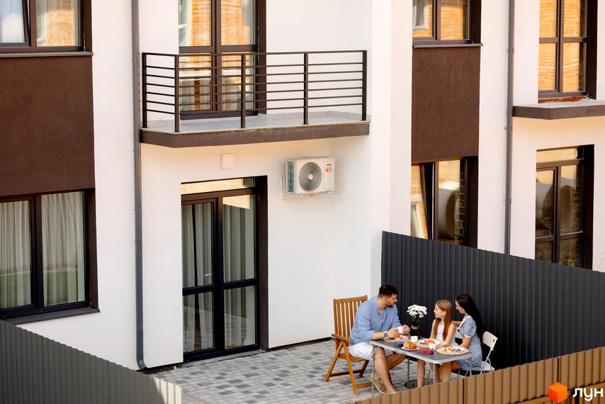 Зовнішній вигляд будинку КМ WEST TOWN XIV з балконом та кондиціонером. Прибудинкова територія з родиною, що снідає на терасі.